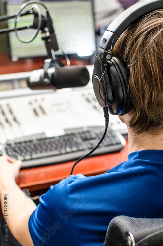 Photo: Dj working in front of a microphone on the radio, from the back Dj working in front of a microphone on the radio, from the back