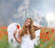 Dreaming angel girl in field of red poppies with white wings
