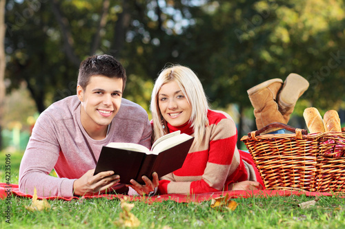 Photo: A loving couple reading a book during a picnic A loving couple reading a book during a picnic