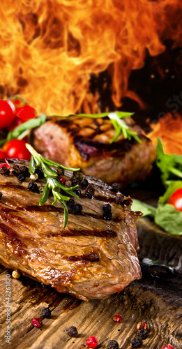 Photo: Grilled beef steaks with flames on background Grilled beef steaks with flames on background
