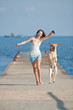 Young woman with Labrador male dog running along the pier
