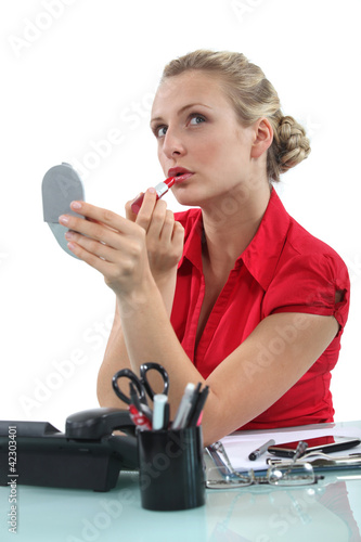 Photo: Blond secretary applying lip-stick at her desk Blond secretary applying lip-stick at her desk