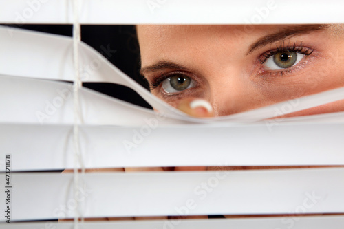 Photo: Woman peering through some blinds Woman peering through some blinds