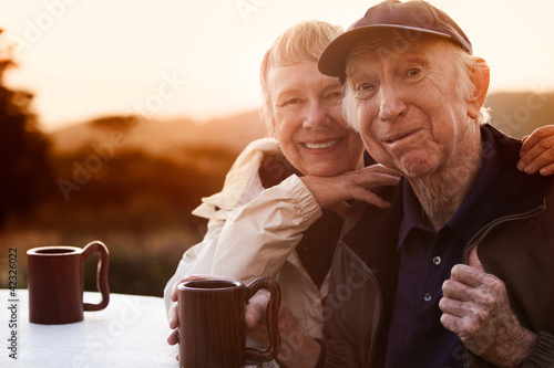 Photo: Cute senior couple in jackets outside at table smiling Cute senior couple in jackets outside at table smiling
