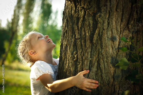 Little girl hugging a tree, looking up