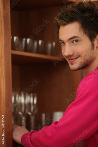 Foto: Young man putting glasses away in a cupboard Young man putting glasses away in a cupboard