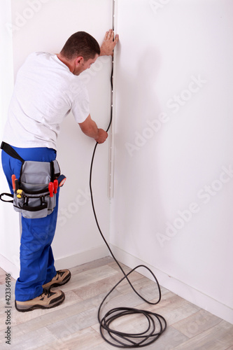 Foto: Electrician fixing a wire to a wall Electrician fixing a wire to a wall