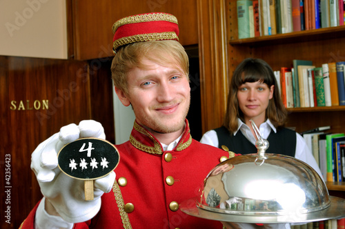 Foto: Hotelpage mit Tafel und Schriftzug 4 Sterne mit Zimmermädchen Hotelpage mit Tafel und Schriftzug 4 Sterne mit Zimmermädchen