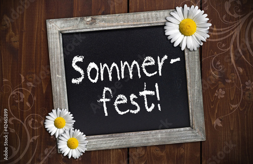 Foto: Kreidetafel mit Sommerfest auf Holzwand und Blüten Kreidetafel mit Sommerfest auf Holzwand und Blüten