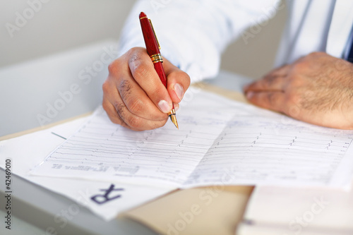 Photo: Hands of a doctor filling RX prescription, documents at the desk Hands of a doctor filling RX prescription, documents at the desk