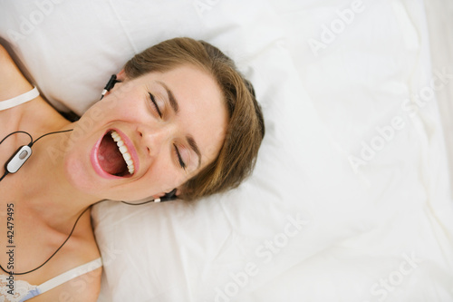 Photo: Portrait of girl in headphones laying on bed and listening music Portrait of girl in headphones laying on bed and listening music