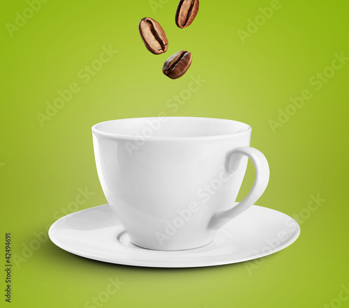 Photo: Coffee cup on green background with coffee beans falling into it Coffee cup on green background with coffee beans falling into it