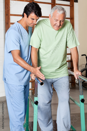 Photo: Therapist Assisting Senior Man To Walk With The Support Of Bars Therapist Assisting Senior Man To Walk With The Support Of Bars
