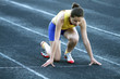 Athletic teenage girl in start position on track .