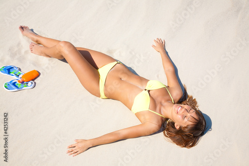Photo: young woman in bikini sunning on the beach young woman in bikini sunning on the beach