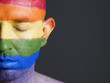 Gay flag painted on the face of a man with closed eyes.