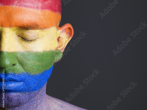 Photo: Gay flag painted on the face of a man with closed eyes. Gay flag painted on the face of a man with closed eyes.