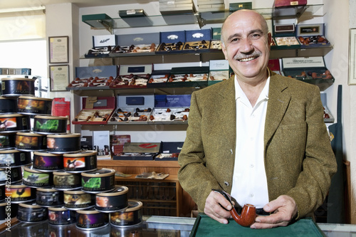 Photo: Portrait of a happy mature tobacco shop owner with cans on display Portrait of a happy mature tobacco shop owner with cans on display