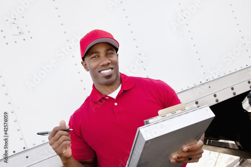 Photo: Portrait of a happy African American man holding clipboard with delivery truck in background Portrait of a happy African American man holding clipboard with delivery truck in background