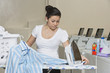 Young female employee ironing clothes in Laundromat