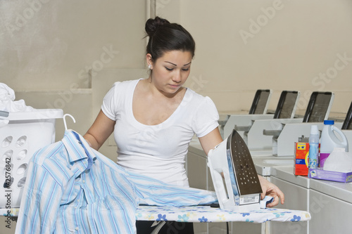 Photo: Young female employee ironing clothes in Laundromat Young female employee ironing clothes in Laundromat