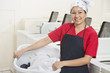 Photo: Portrait of a happy young female employee carrying laundry basket with washing machines in background Portrait of a happy young female employee carrying laundry basket with washing machines in background