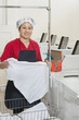 Photo: Portrait of a happy woman wearing uniform holding clothes with washing machines in background Portrait of a happy woman wearing uniform holding clothes with washing machines in background