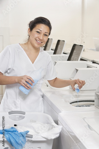 Photo: Portrait of a happy woman employee pouring detergent in washer Portrait of a happy woman employee pouring detergent in washer