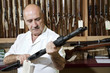 Foto: Mature gun shop merchant looking at rifle in store Mature gun shop merchant looking at rifle in store