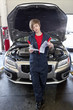 Young female mechanic reading paper with open bonnet of car in garage