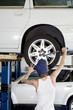 Back view of young female working on car tire in workshop