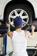Back view of young female mechanic working on lifted car's tire in automobile repair shop