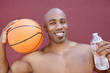 Photo: Portrait of an African American athlete with basketball and water bottle over colored background Portrait of an African American athlete with basketball and water bottle over colored background