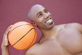 Photo: Young African American man with basketball on shoulder looking away over colored background Young African American man with basketball on shoulder looking away over colored background