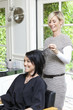 Cheerful hairstylist looking at hair of beautiful woman in beauty salon