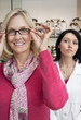 Photo: Portrait of a happy woman trying glasses with optician in background Portrait of a happy woman trying glasses with optician in background