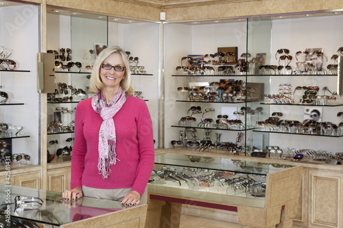 Photo: Portrait of a happy senior female optician standing in store Portrait of a happy senior female optician standing in store
