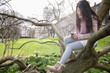 Young woman sitting on tree branch while text messaging