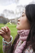 Side view of a young Asian woman smelling flower in park