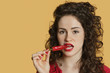 Photo: Portrait of a young woman biting red chili pepper over colored background Portrait of a young woman biting red chili pepper over colored background
