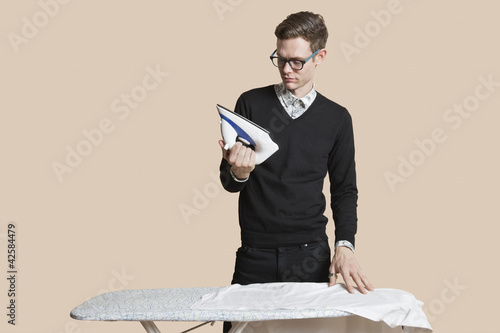 Photo: Mid adult man looking at iron over colored background Mid adult man looking at iron over colored background