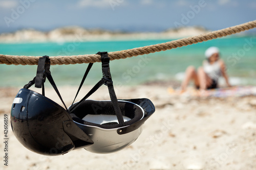 Photo: Helmets on the beach. Young woman relaxing on the background. Helmets on the beach. Young woman relaxing on the background.