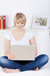 blonde frau sitzt mit laptop auf dem sofa