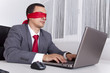 Foto: Blindfold businessman working with his laptop Blindfold businessman working with his laptop