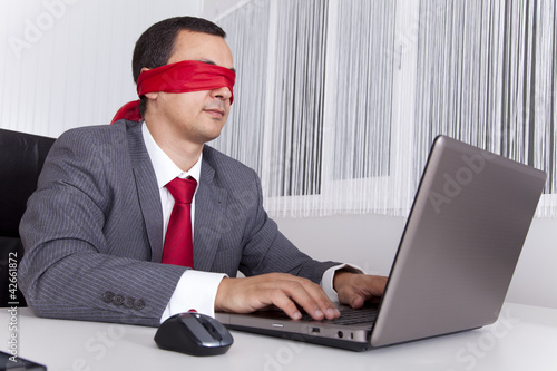 Photo: Blindfold businessman working with his laptop Blindfold businessman working with his laptop