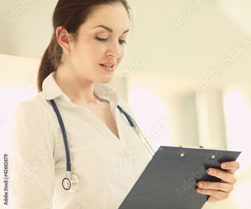 Photo: A smiling female doctor with a folder in uniform indoors A smiling female doctor with a folder in uniform indoors