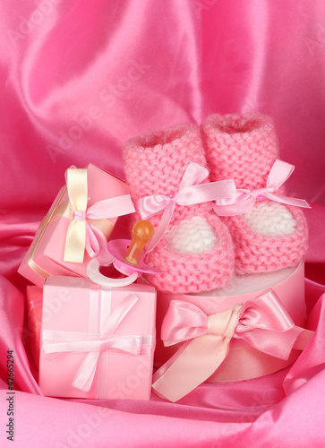 Foto: pink baby boots, pacifier, gifts on silk background. pink baby boots, pacifier, gifts on silk background.