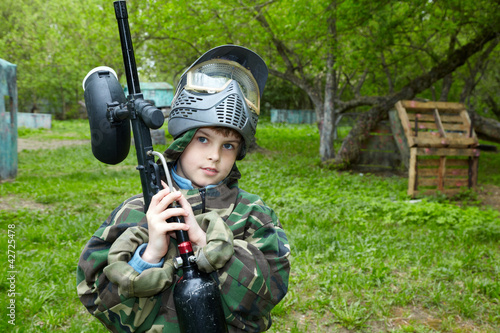 Photo: Boy in camouflage suit stands against the paintball area Boy in camouflage suit stands against the paintball area