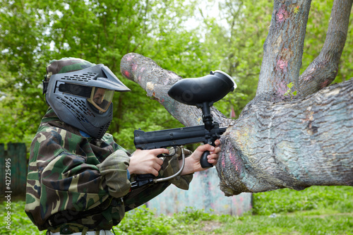Photo: Paintball player in camouflage uniform and protective mask aims Paintball player in camouflage uniform and protective mask aims