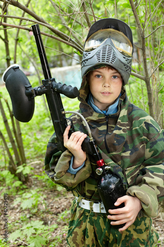 Photo: Boy in camouflage stands against brushes on paintball area Boy in camouflage stands against brushes on paintball area